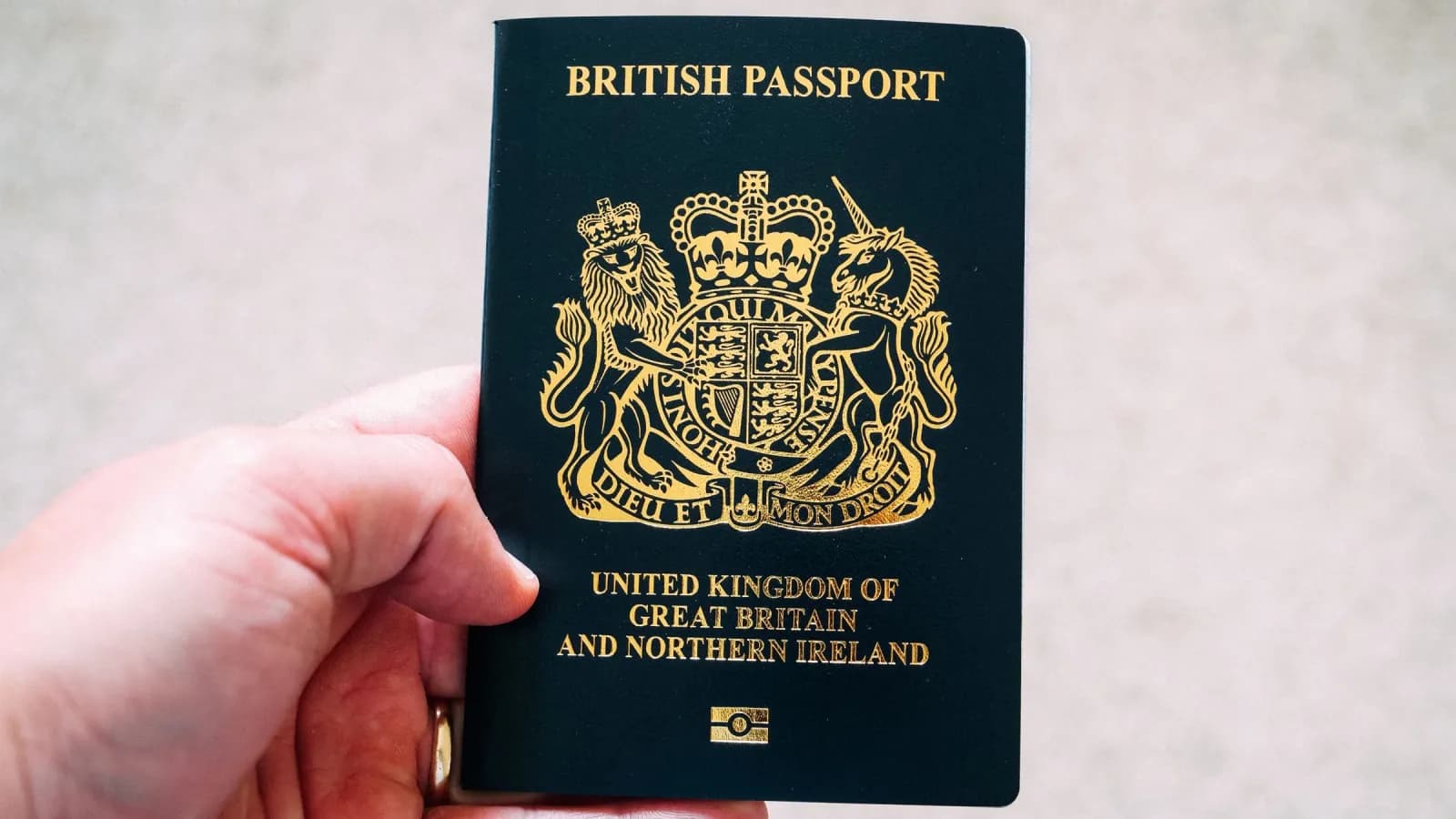 A hand holding a dark blue British passport against a plain pale background.