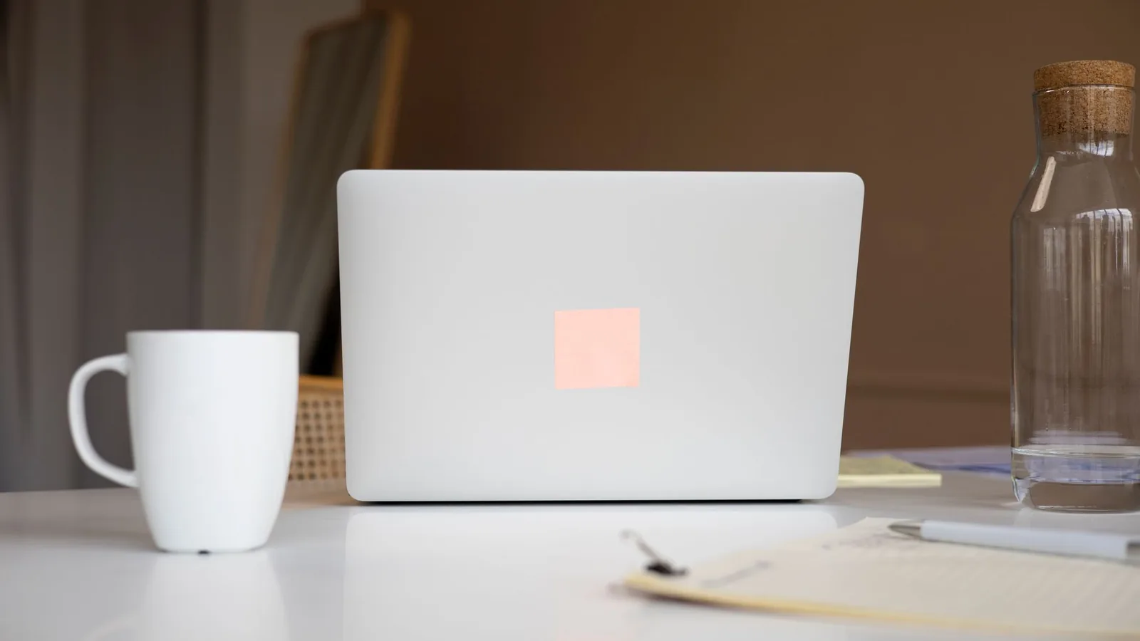 Modern minimalist workspace with a laptop, ceramic mug, and glass water bottle on a white surface