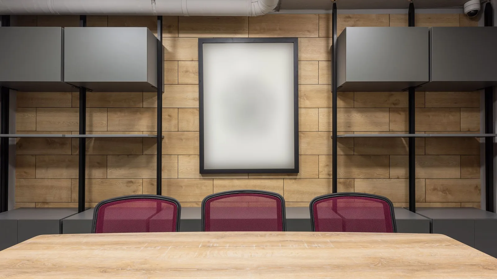 Three red chairs at a wooden meeting table in an empty boardroom