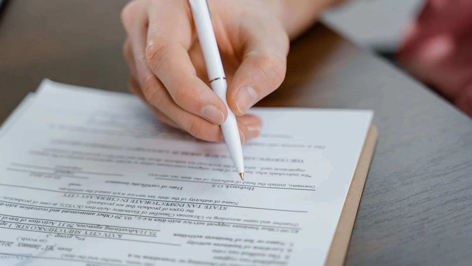 A hand holding a pen signing a document, close up shot with focus on the paper