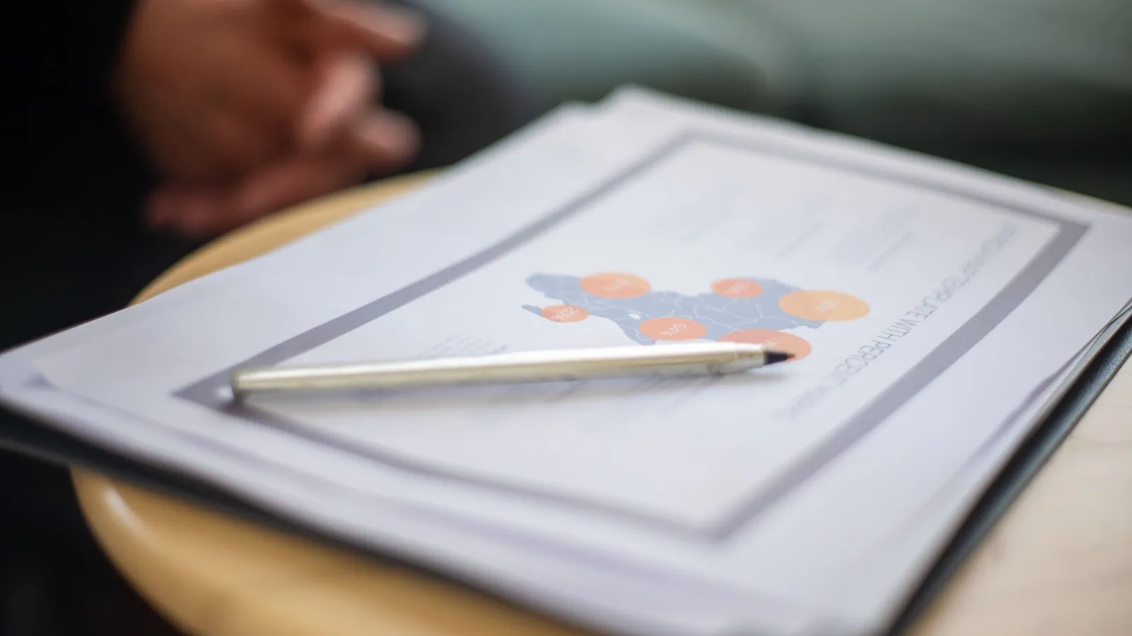 A silver pen resting on a printed business report with a map chart, on a round wooden table