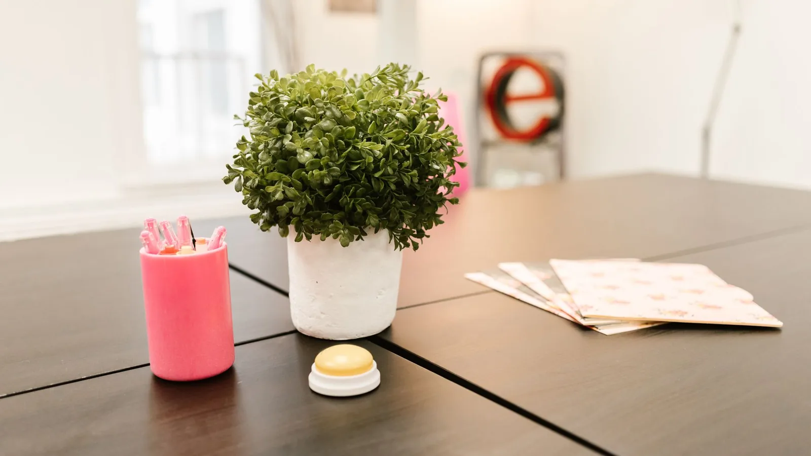 A potted plant, a pot of pens and a few folders on a dark meeting table